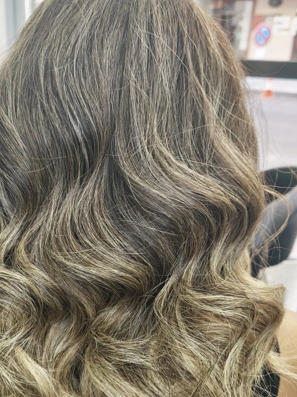 Después del balayage: la raíz se funde en un rubio beige sin línea de corte, con la melena en ondas, vista de espaldas